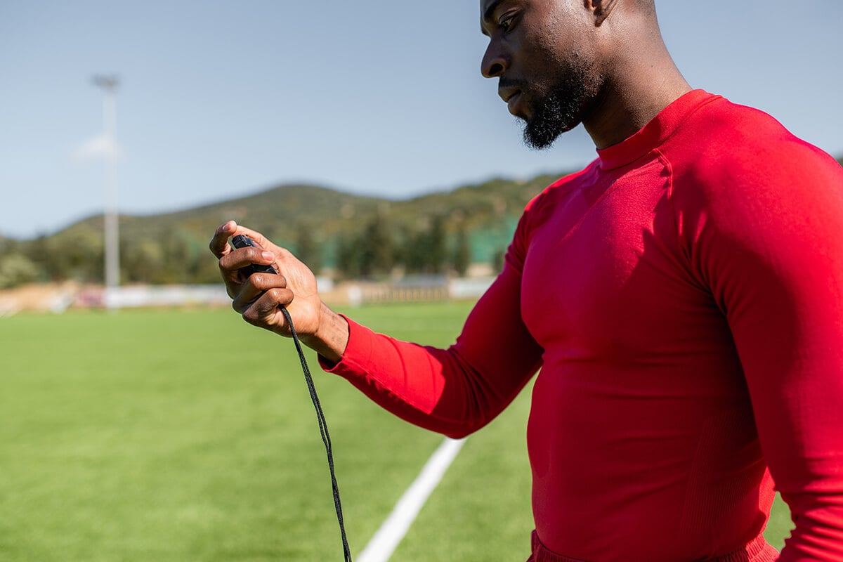 A Man in a Red Top Holding a Stop Watch on a Sports Field