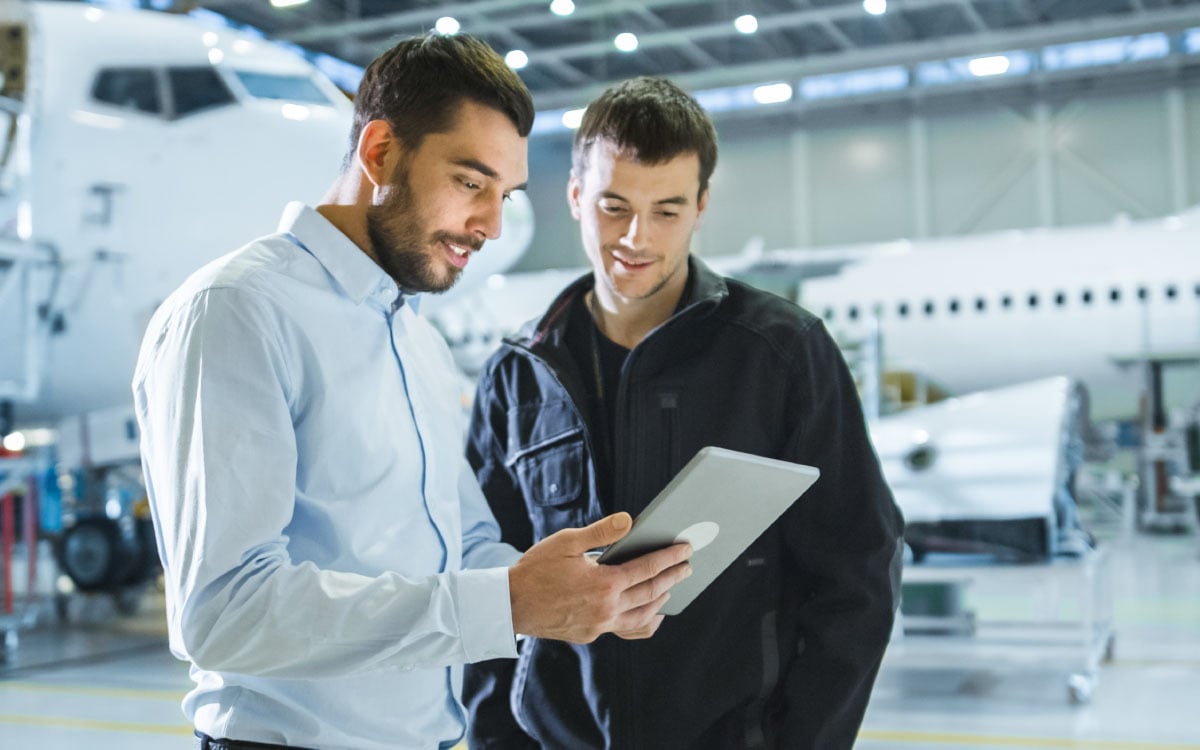 Two men looking at a tablet in a room with aircrafts