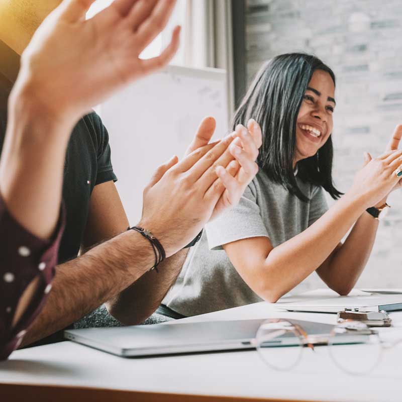 Two People Sat at a Table Smiling and Clapping their Hands