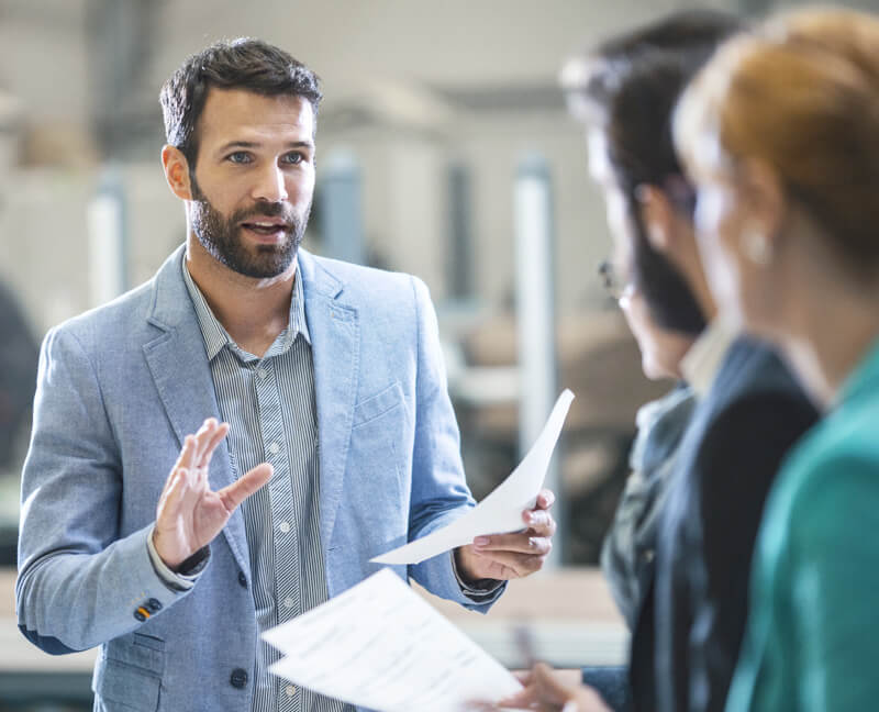 A Man Holding a Piece of Paper and Talking to Three Other People