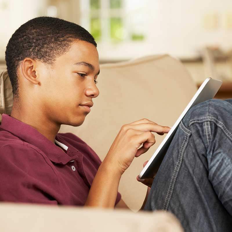 A Boy Looking at a Tablet Whilst Sat on a Sofa